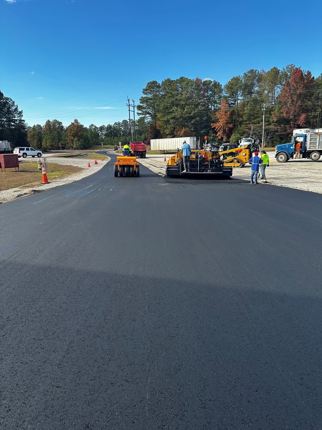 Fresh hot-mix asphalt being laid by a paver with trees in the background